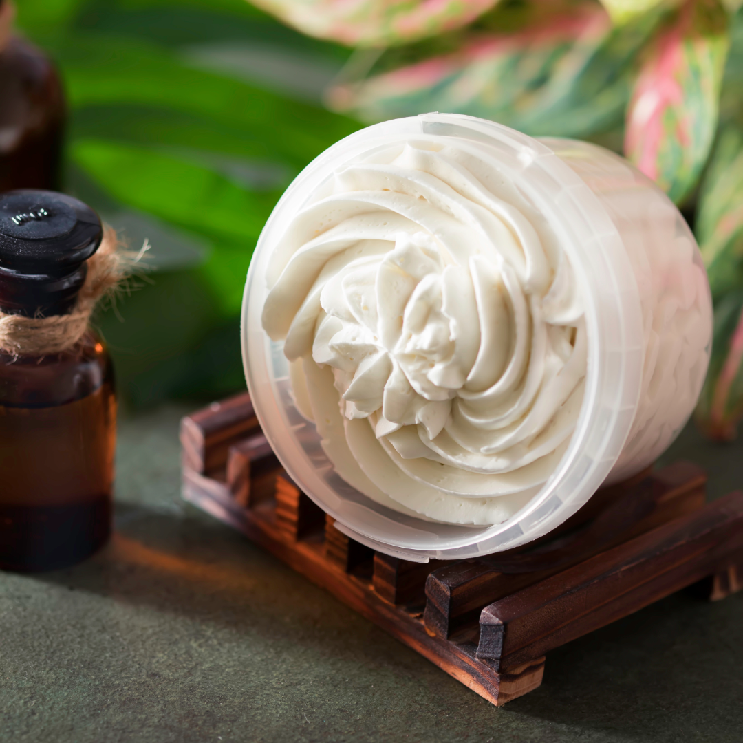 White whipped lavender body butter on a wooden stand with green leaves in the background by House of Agave.