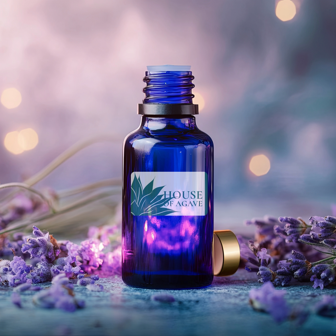 Blue bottle of pure lavender essential oil, with House of Agave label, surrounded by lavender flowers on a blurred background.